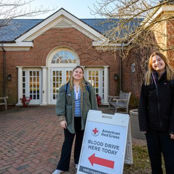 Two students standing in front of building next to sign advertising American Red Cross blood drive